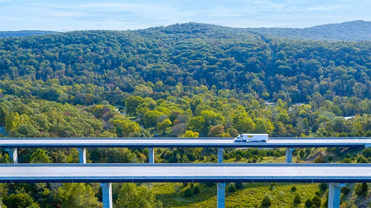 Enterprise Wide Sustainability Campaign Blog Header Photo of a J.B. Hunt semi truck and trailer crossing a bridge over a hilly landscape