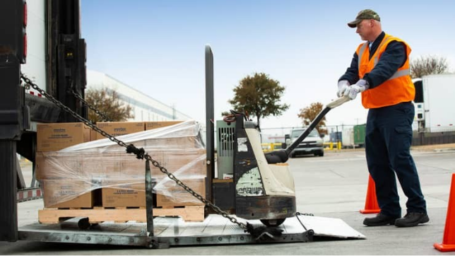 Person in a high visibility vest unloads a truck with a pallet cart